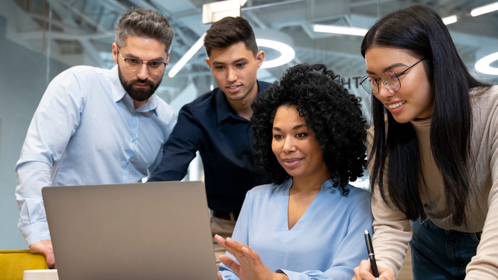Équipe de quatre collègues réunie autour d'un ordinateur portable dans un bureau